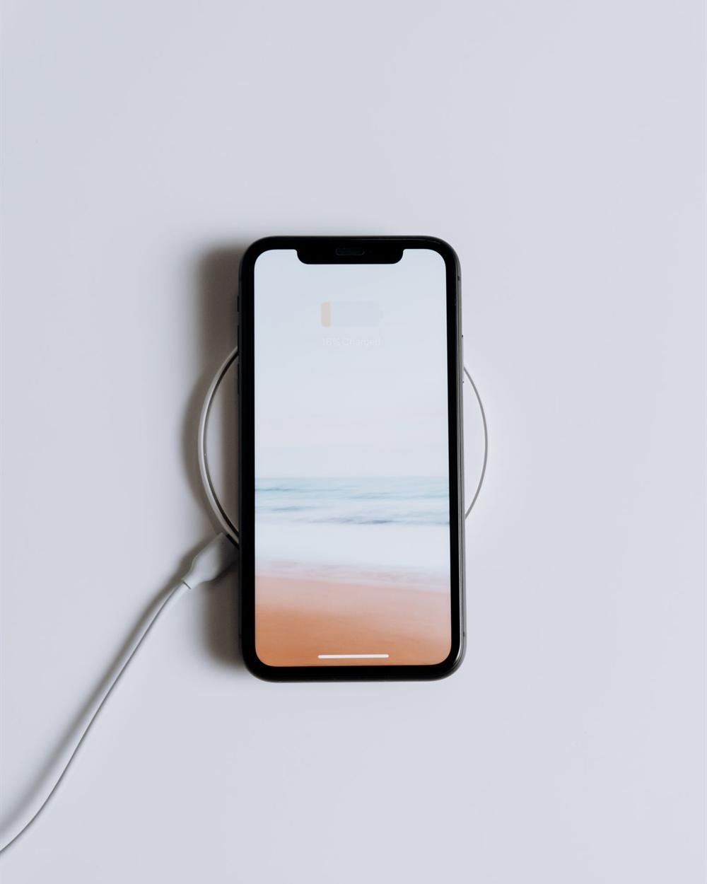 A smartphone charging on a round wireless charger on a white table