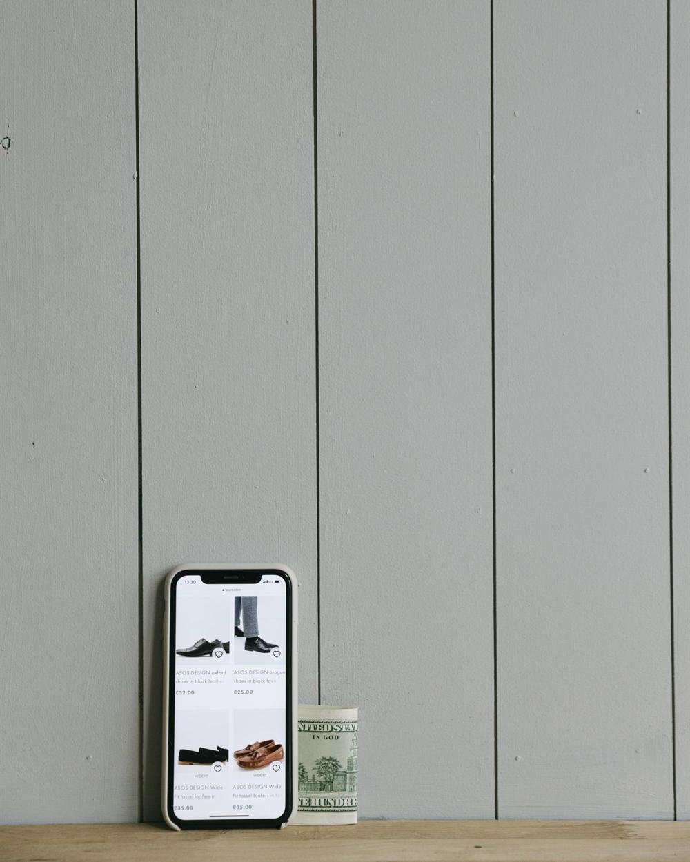 A smartphone standing next to a roll of cash against a wooden wall