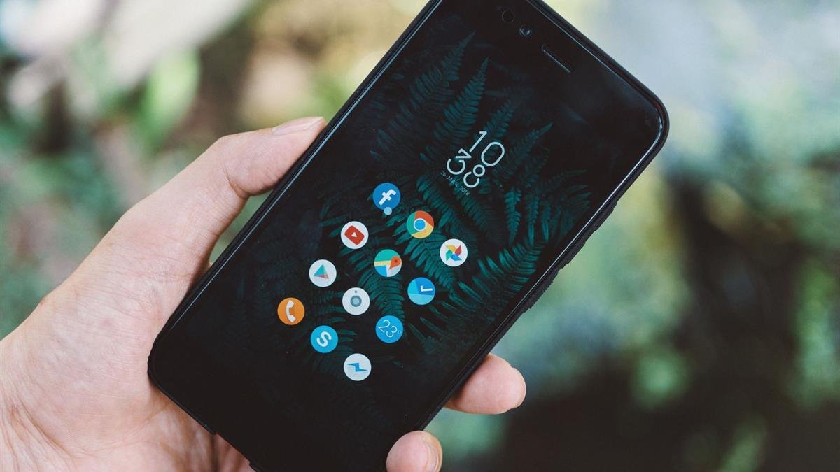 A hand holding a black Android phone showing its home screen