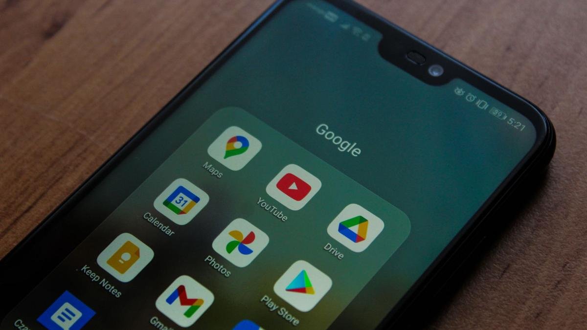 A black Android phone on a wooden table showing a folder of Google apps