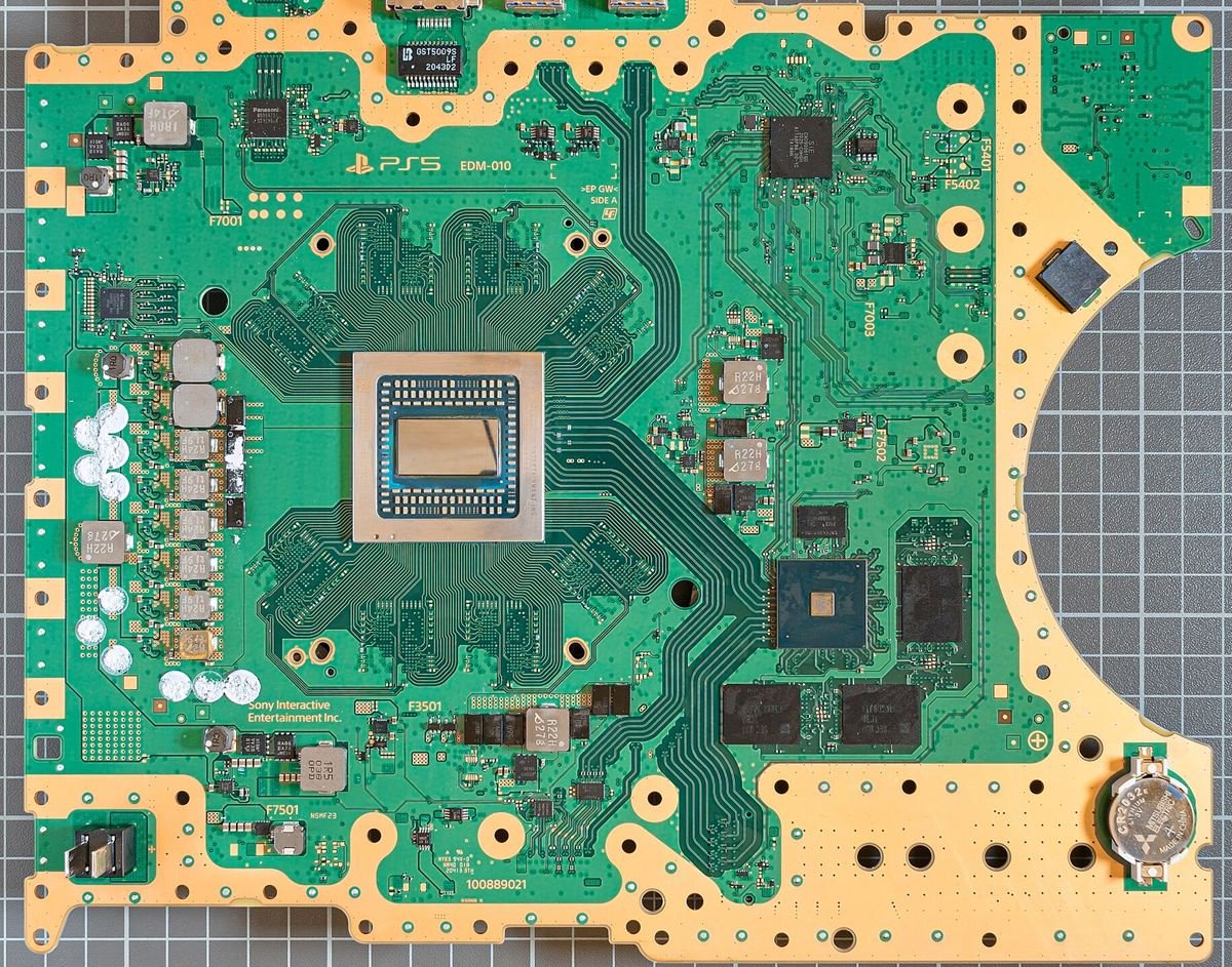 A PS5 motherboard with the cooler removed, showing the large main chip in the centre