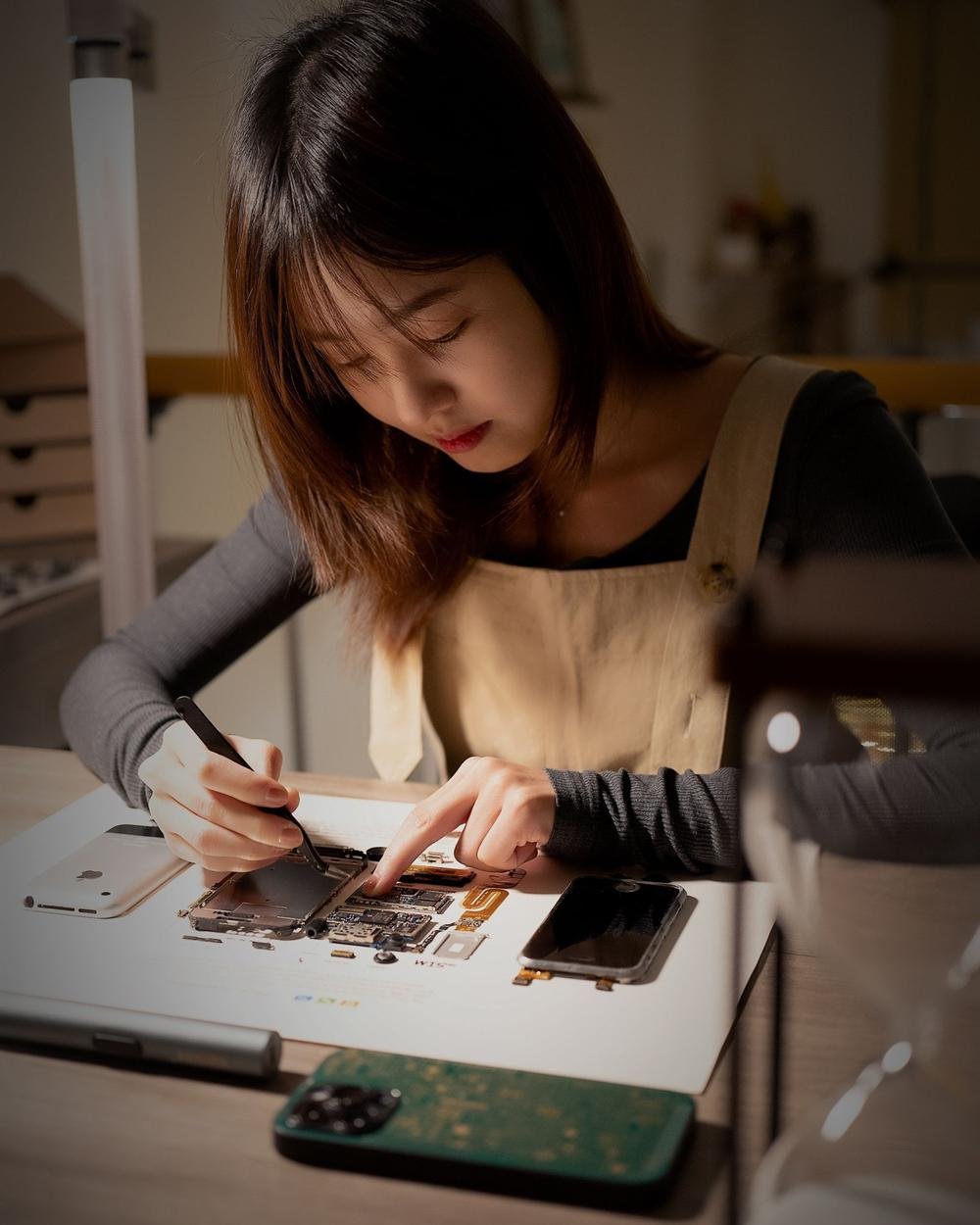 A woman working on a phone that has been taken apart on a workshop desk