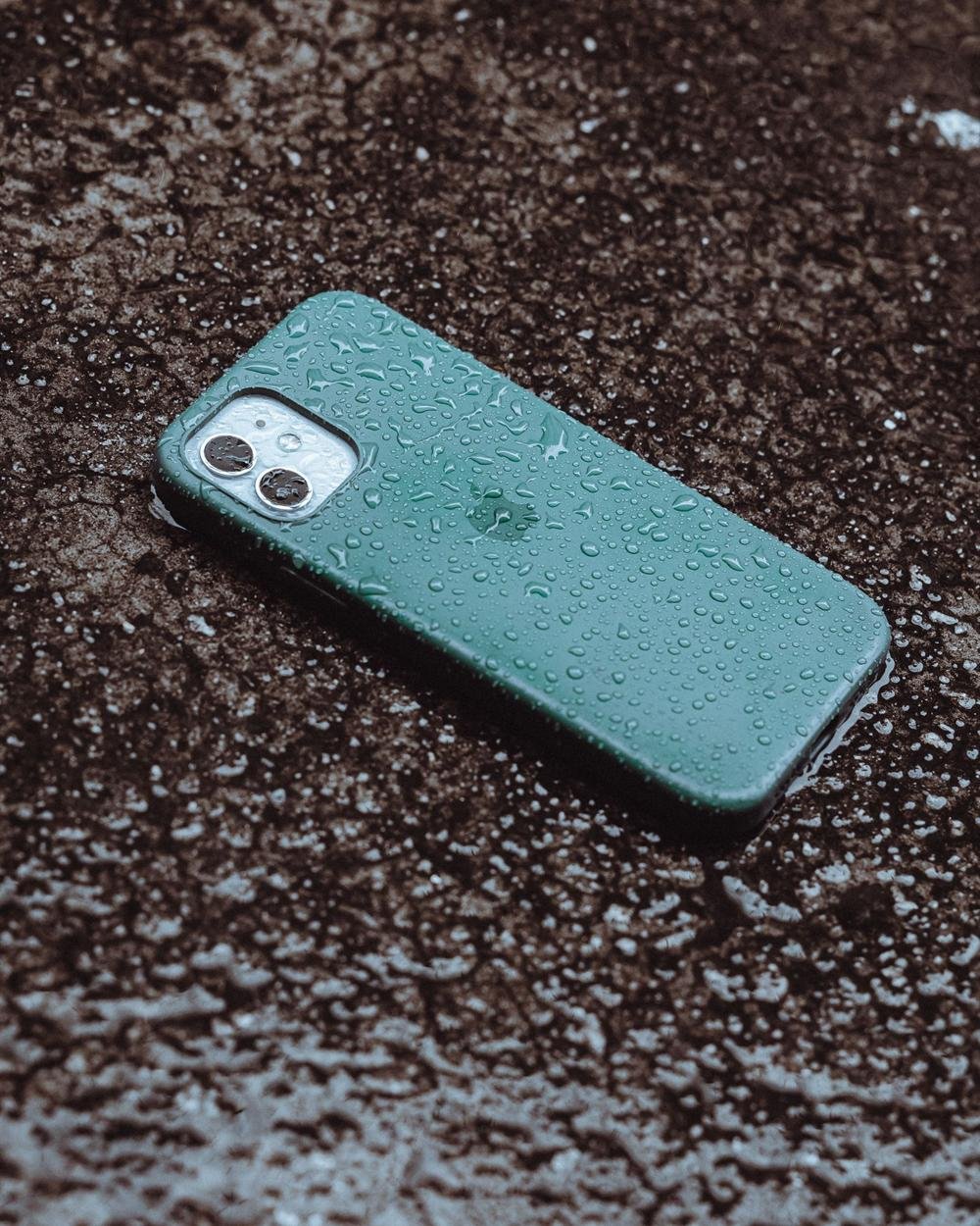 A phone lying on wet ground covered in raindrops