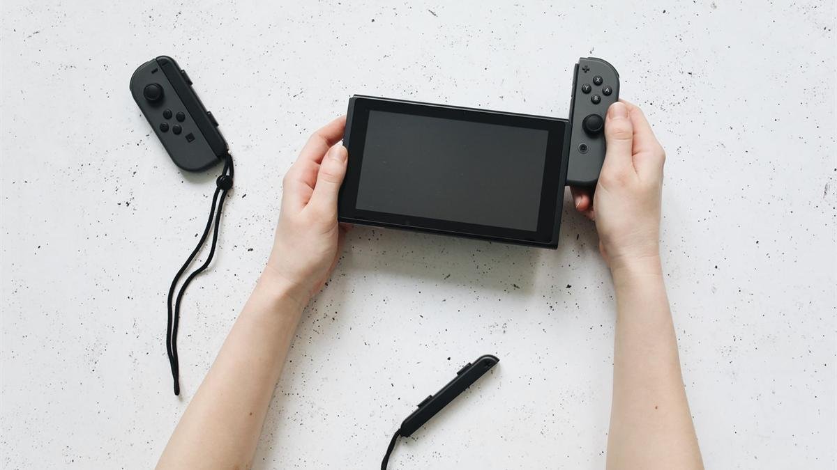 A Nintendo Switch held in two hands with one Joy-Con controller detached